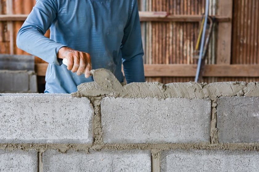 Person laying concrete blocks with a trowel at a construction site