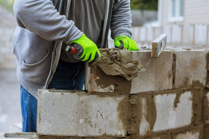 Worker in neon gloves spreading mortar on a cinder block wall under construction