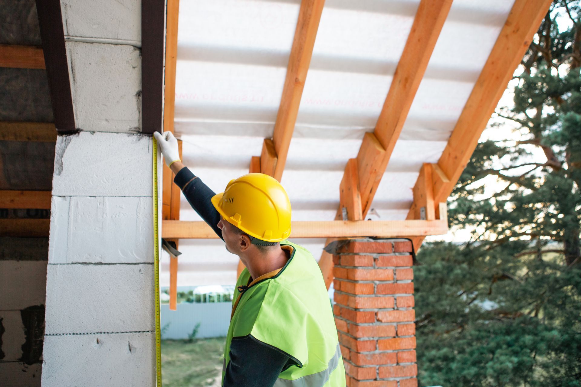 Worker in yellow hard hat installing insulation under a roof frame at a construction site
