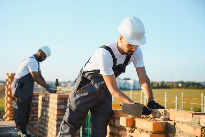 Construction workers laying bricks on a wall outdoors under a clear sky
