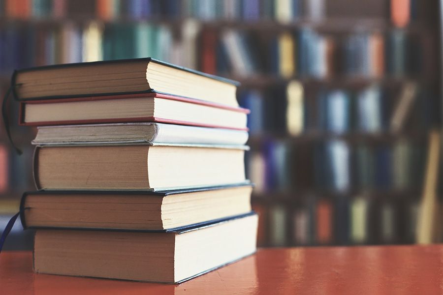 Stack of hardcover books on a wooden table with a blurred bookshelf background.