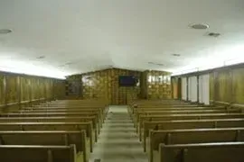 Empty church interior with wooden pews, central aisle, and altar at the front.