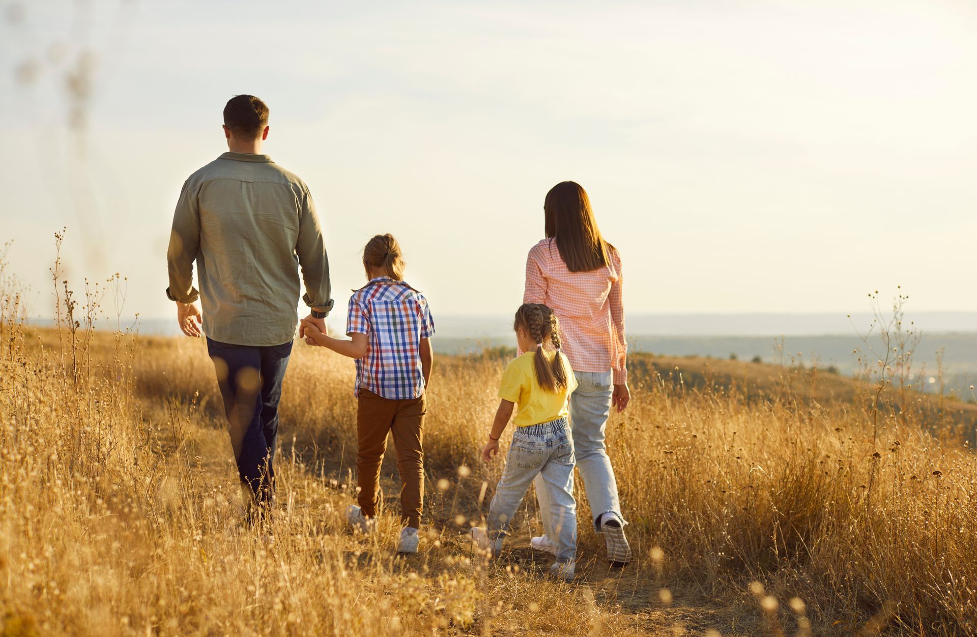 Family walking through a sunlit field of tall dry grass at sunset