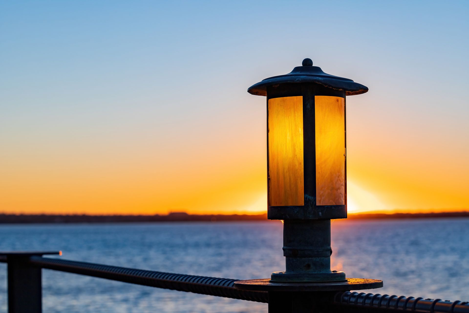Lantern silhouetted at sunset over calm water, with orange glow on the horizon