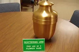 Brass urn on a table with a sign reading “scattering urn, then use as flower vase.”