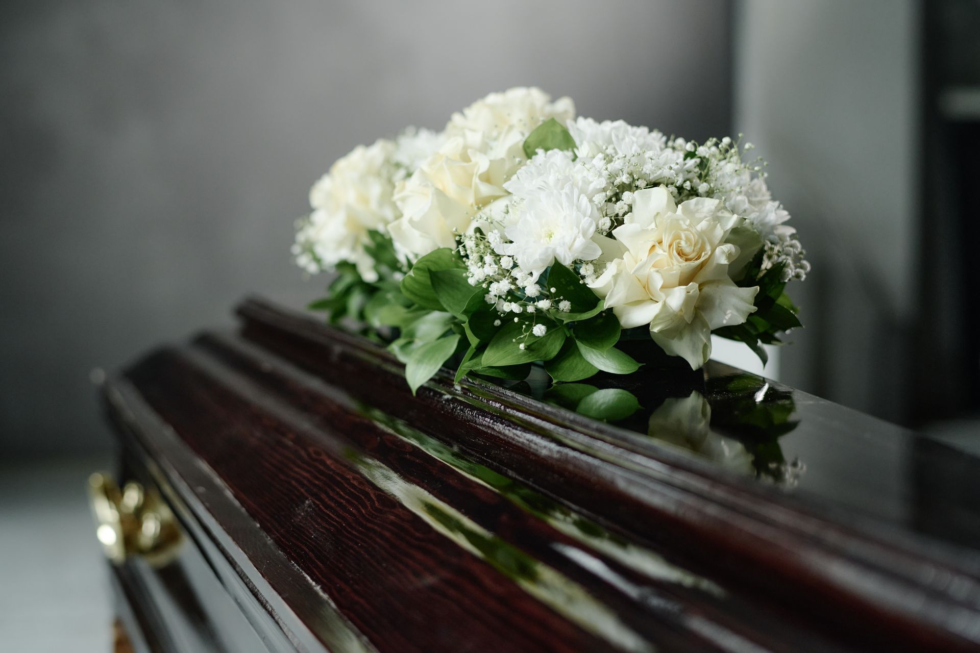 White flowers arranged on a dark polished casket in a funeral setting