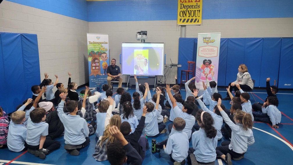 A group of uniformed school children enthusiastically raising their hands during a presentation.