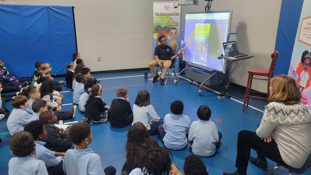 Myles Nobles sitting on a chair engaging with attentive school children during a reading session.