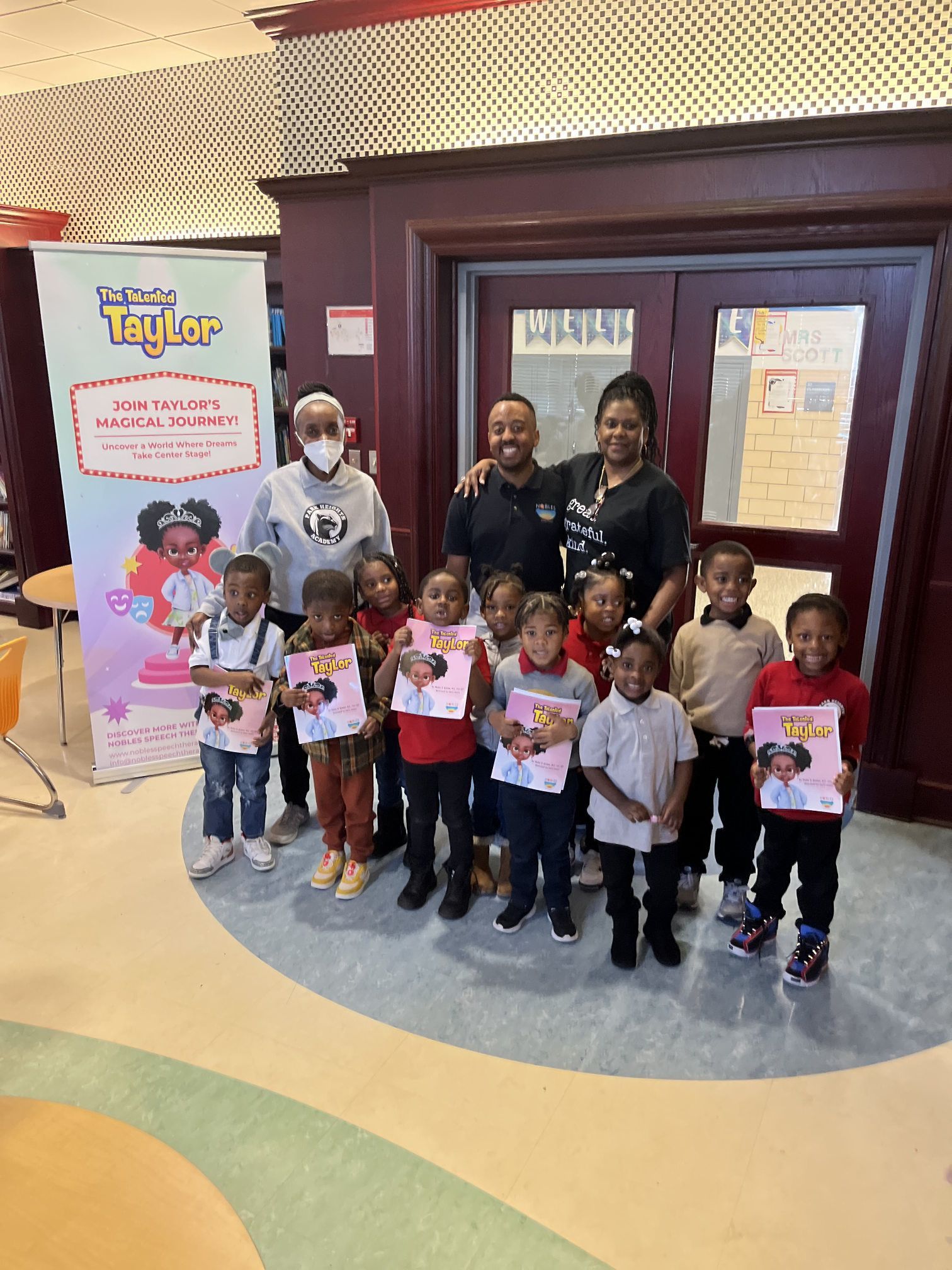 A group of children and adults smiling for a photo in a school library with a