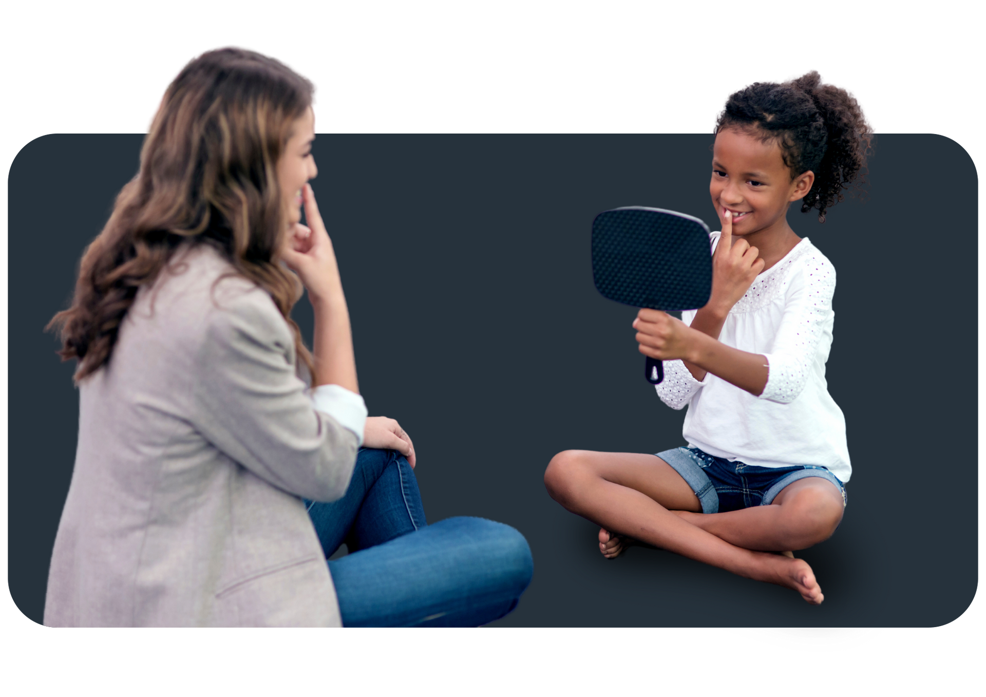 A woman is sitting next to a little girl who is looking at herself in a mirror.