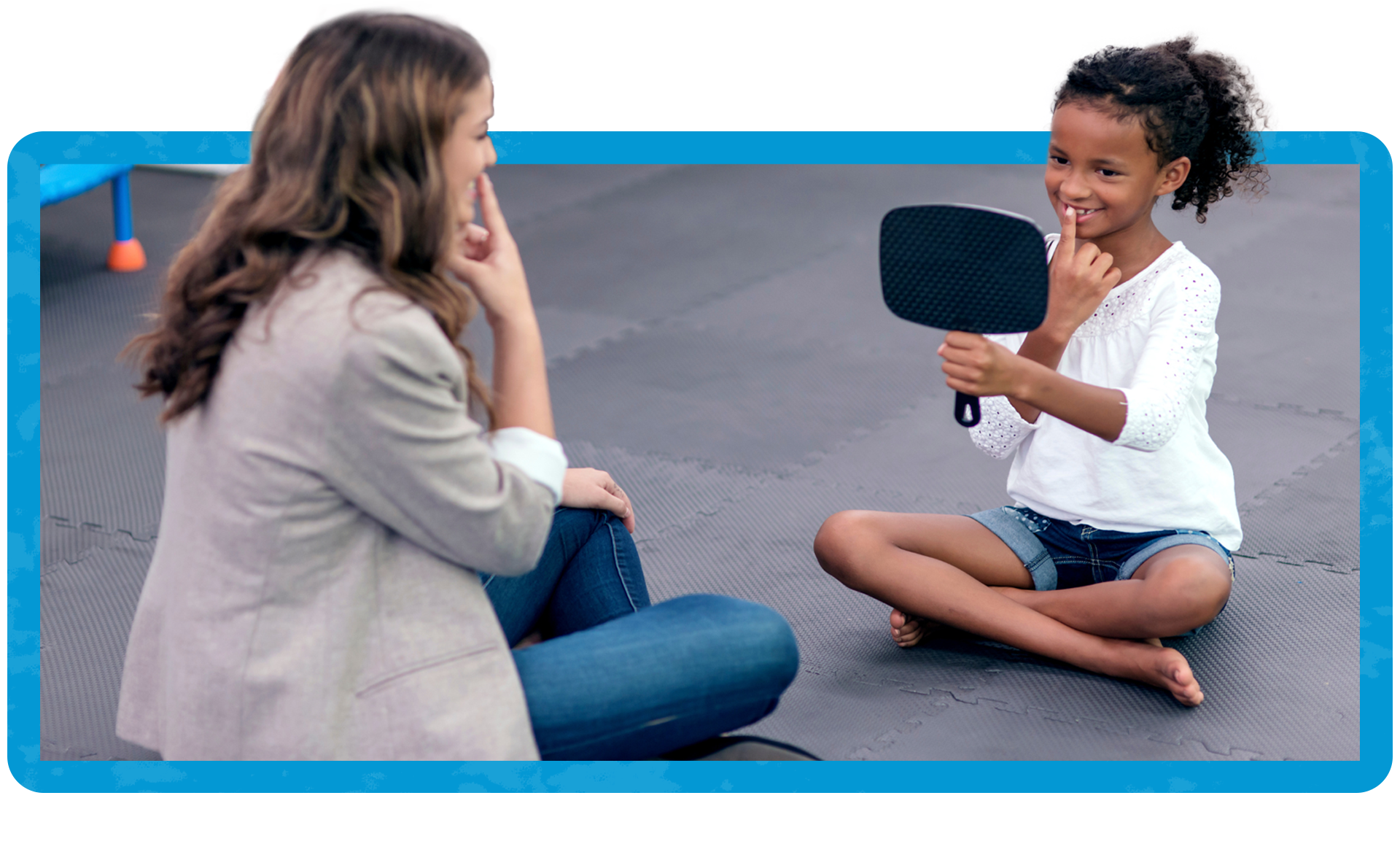 A girl looking at the mirror as she was talking to a speech therapist