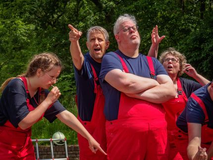 People in red overalls cheering outdoors, with one person eating and another pointing.
