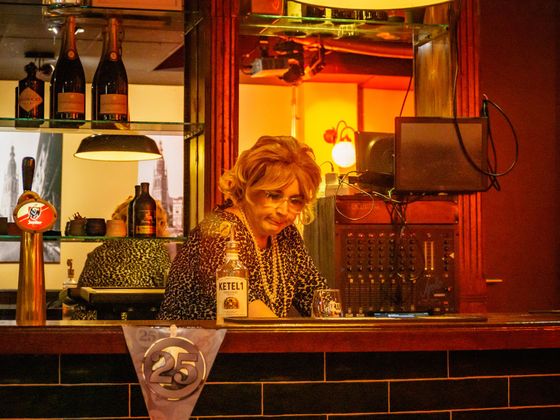 Bartender behind a warmly lit bar, looking down among bottles and glassware.