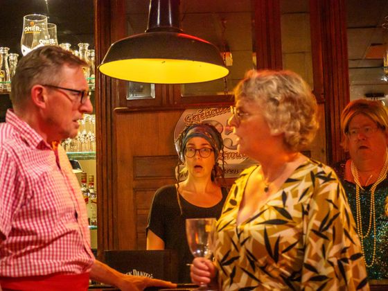People chatting under a hanging lamp in a warmly lit bar or restaurant.