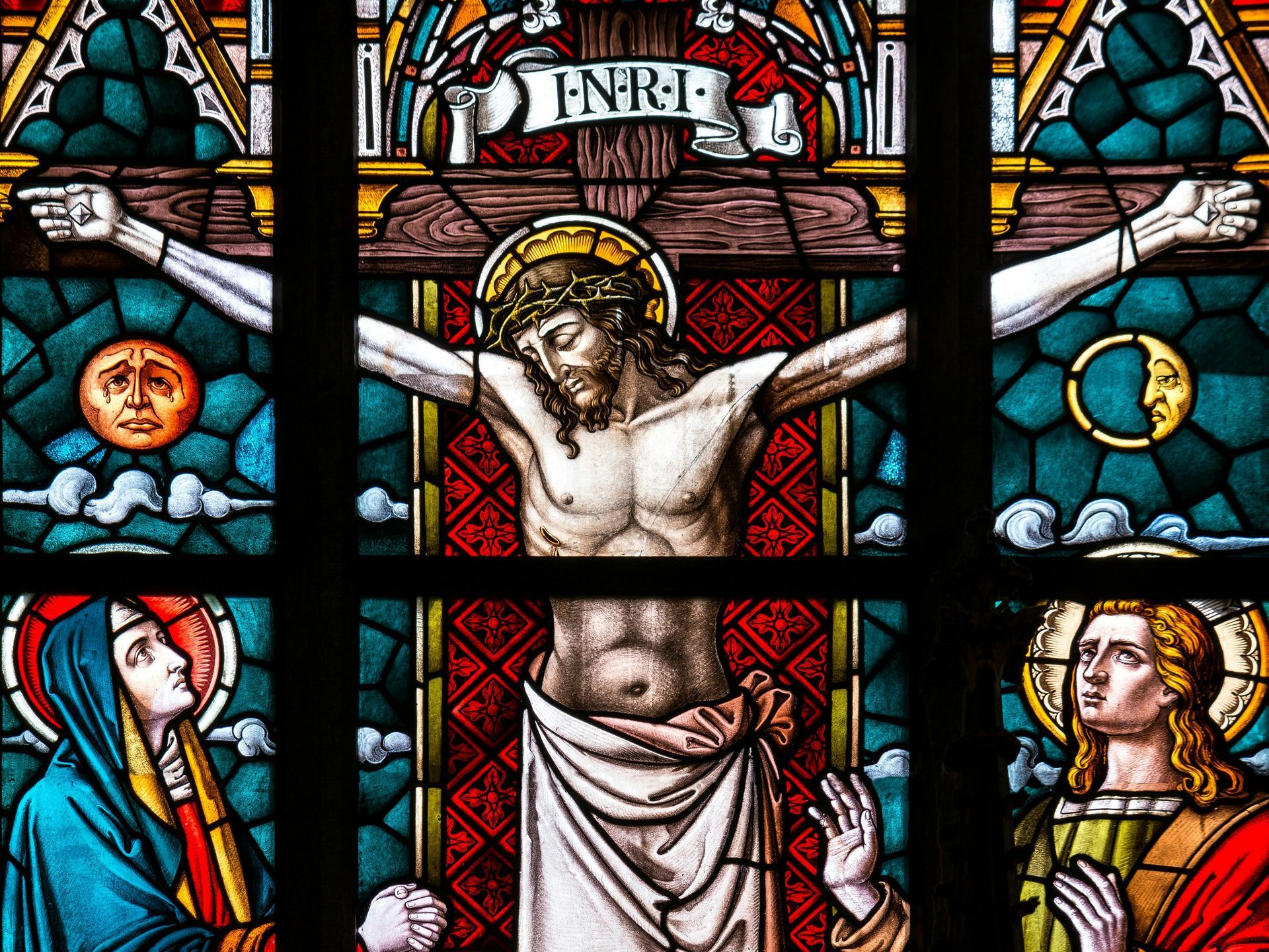 Stained glass of Jesus on the cross, crowned with thorns. Figures below, sun and moon flanking.
