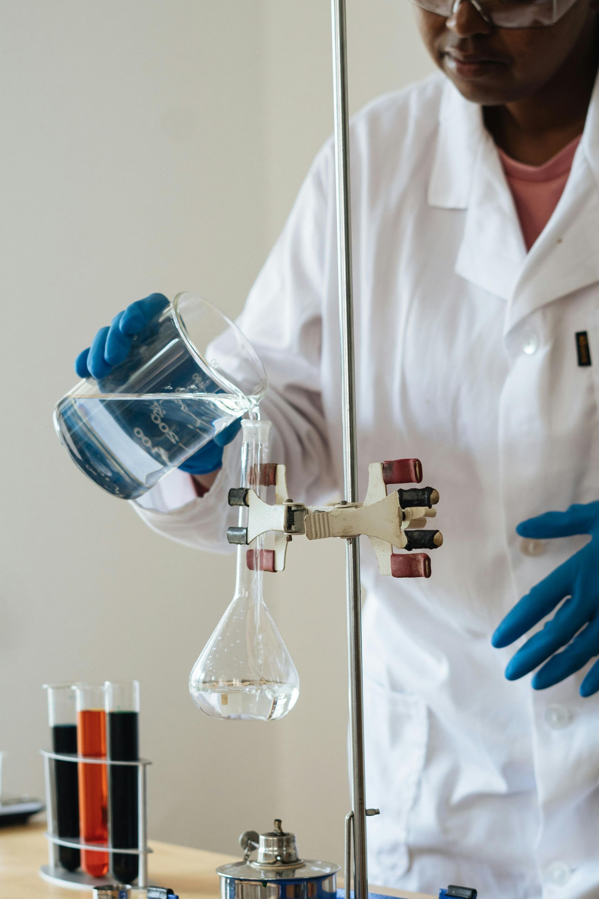 A woman in a lab coat is pouring liquid into a beaker.