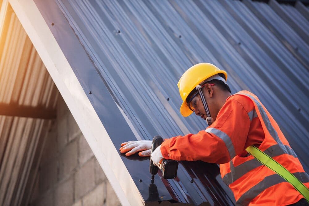 A Construction Worker Is Installing a Metal Roof on A Building — Roof Masters NQ in Douglas, QLD