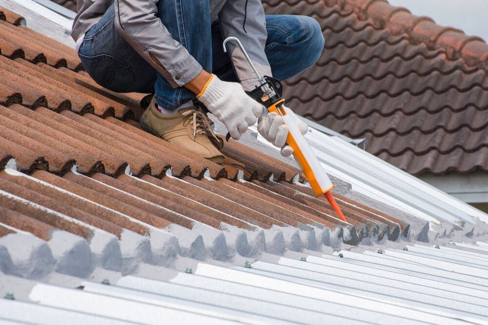 A Man Is Kneeling on Top of A Roof Applying Sealant to It — Roof Masters NQ in Douglas, QLD