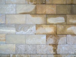 Close-up of a beige and gray stone brick wall with textured rectangular blocks