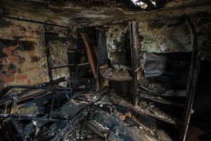 Charred, fire-damaged room with burned debris, blackened walls, and collapsed shelving