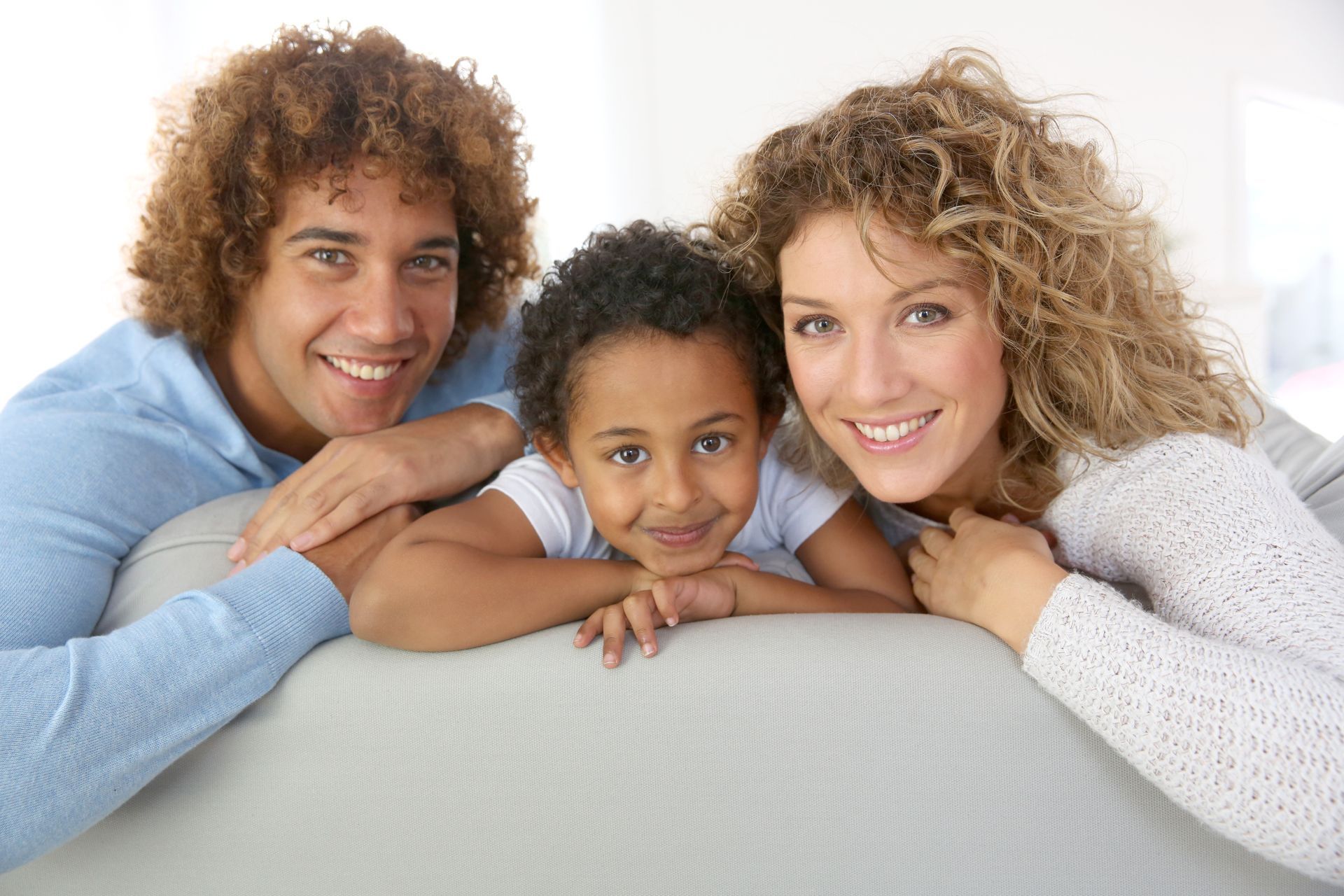 Three people smiling and leaning over a white couch in a bright room