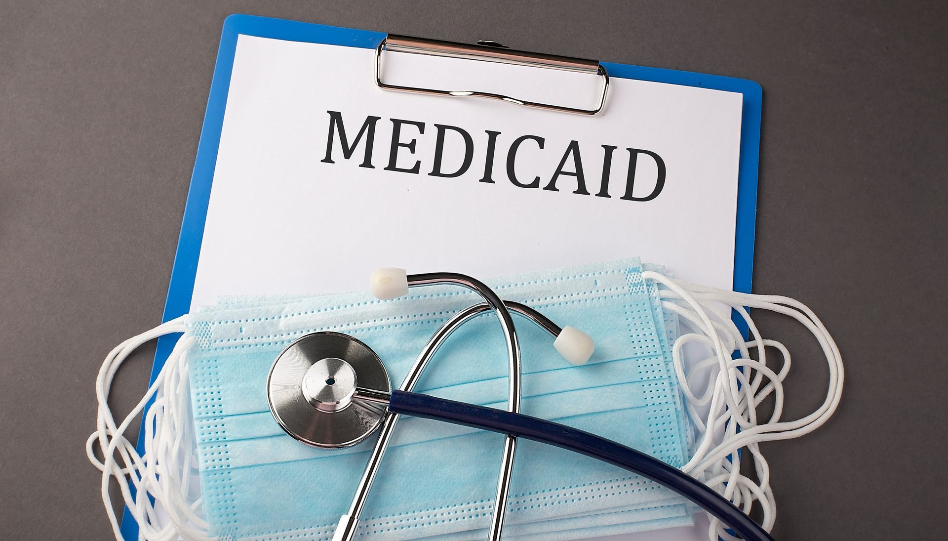 Clipboard labeled “MEDICAID” with a blue surgical mask and stethoscope in front