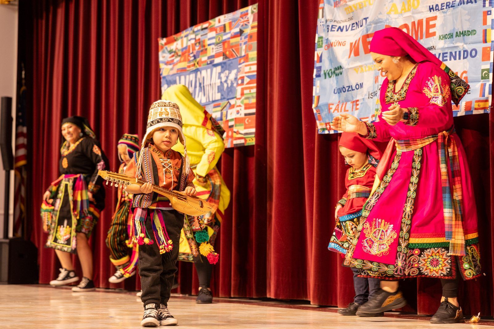 Children in colorful traditional costumes performing on a stage with red curtains