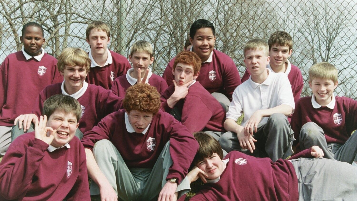 Students in maroon school uniforms posing outdoors in front of a chain-link fence