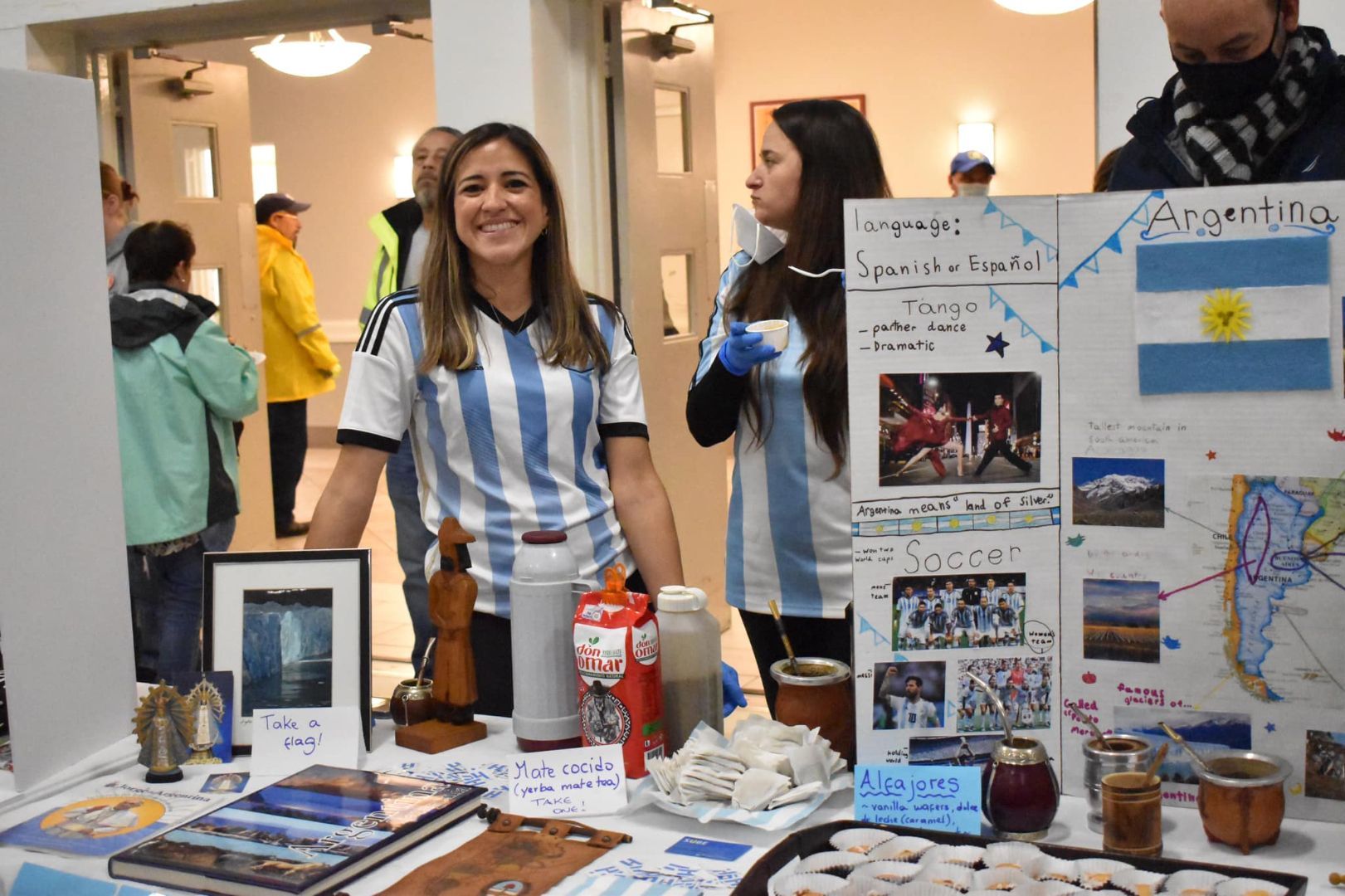 Woman at a booth with posters, books, and crafts on a display table at an indoor event