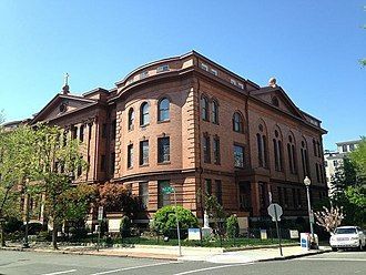 Brick historic building on a sunny street corner with trees and parked cars