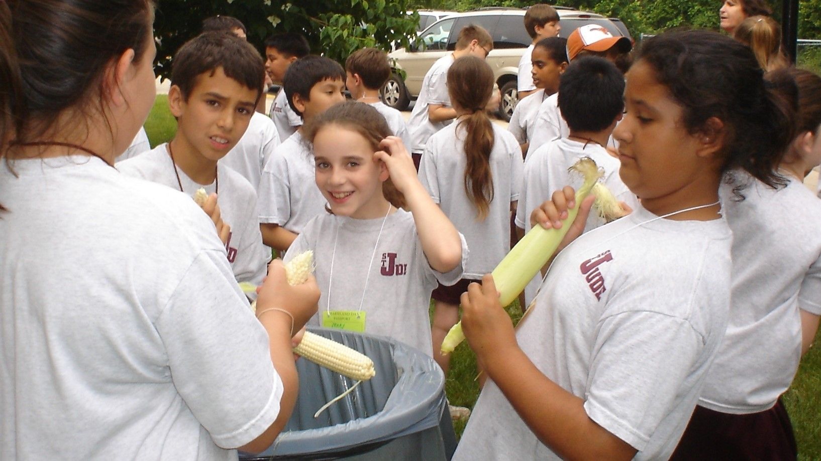 Students in white shirts gather outdoors, holding yellow pool noodles and chatting in a group.