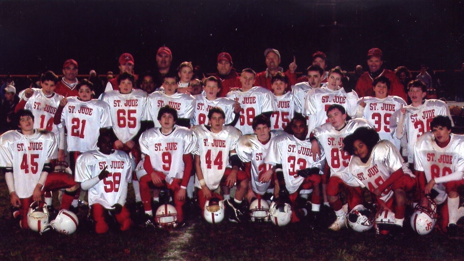 Football team posing for a group photo in white and red uniforms at night