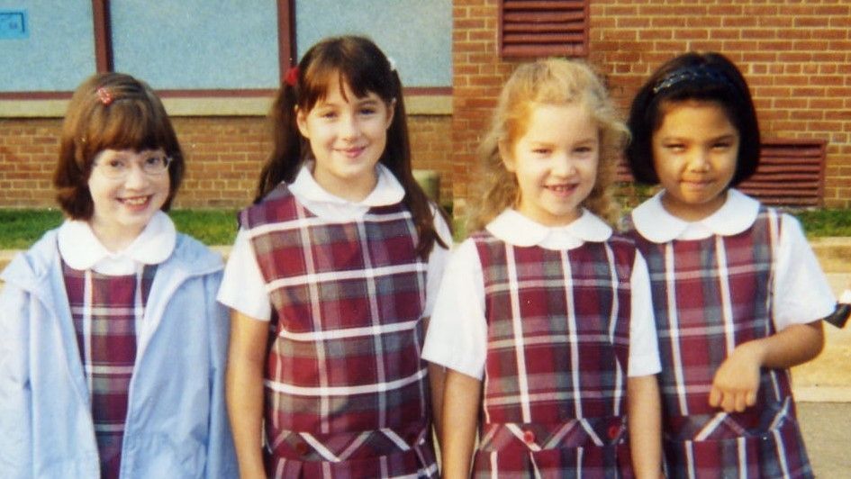 Four schoolchildren in plaid uniforms stand side by side outside a building.