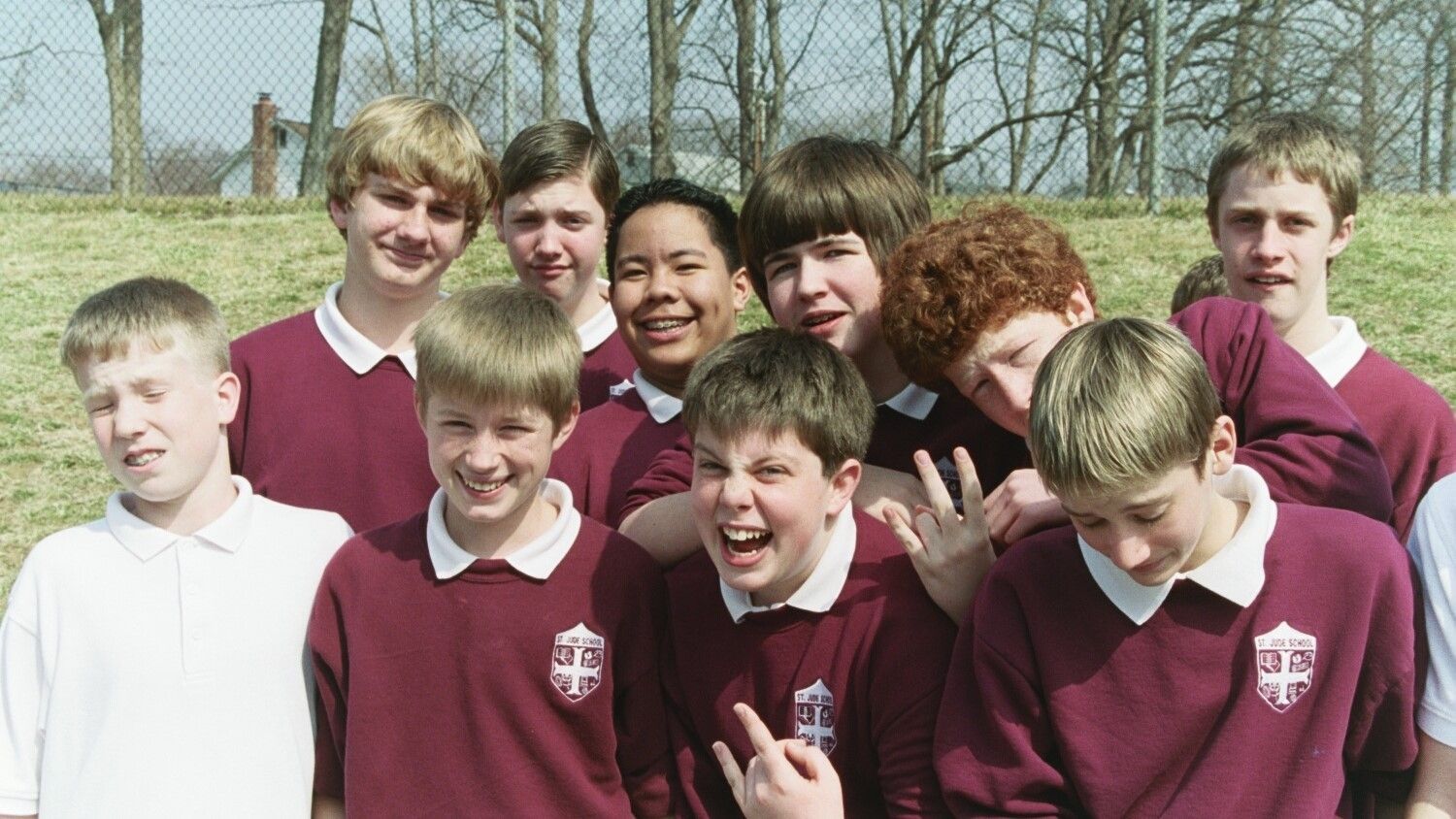 Group of students in maroon school sweaters smiling outdoors on a sunny day