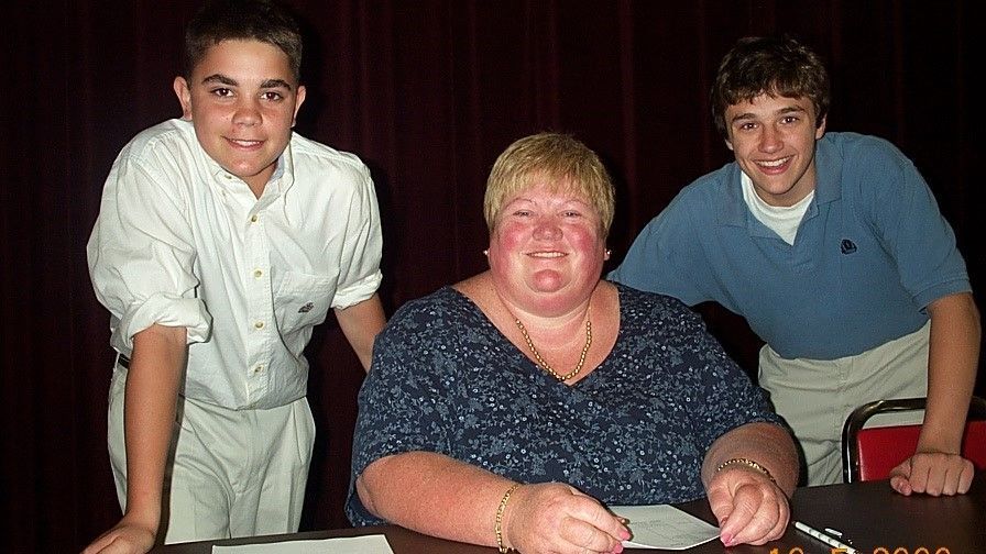 Three people posing at a table, with a cake in front of the seated person.