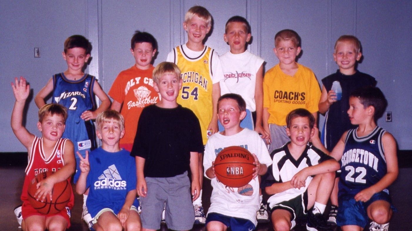 Youth basketball team posing in jerseys, one player holding a basketball and others smiling indoors