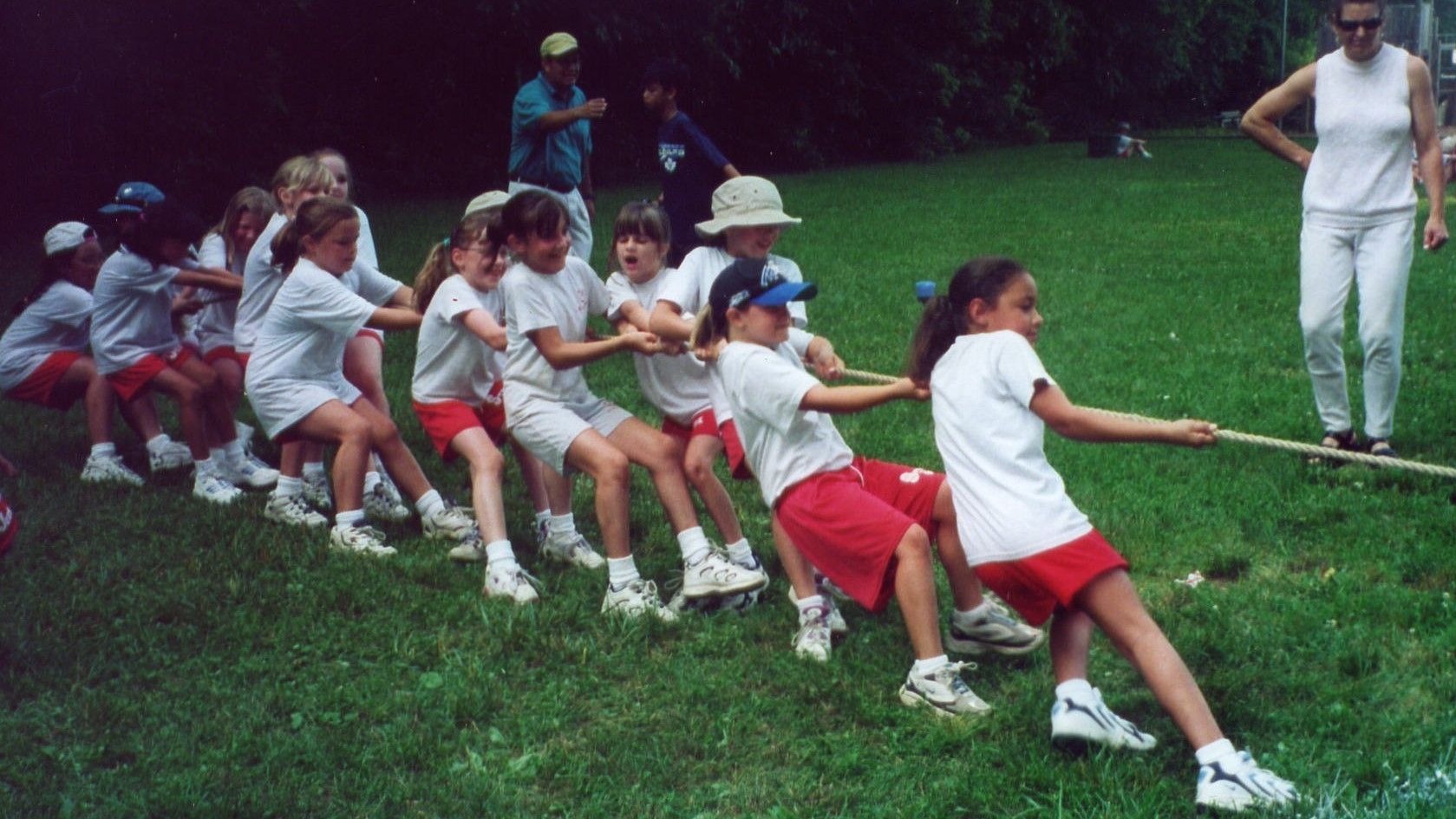 Children in white and red uniforms tugging a rope in a grassy outdoor tug-of-war game