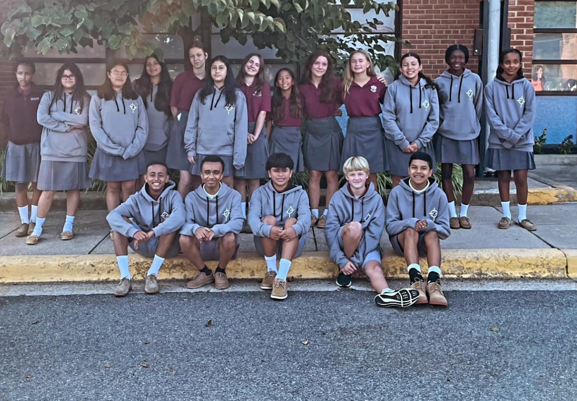 Group of students in gray uniforms posing outside a brick school building.