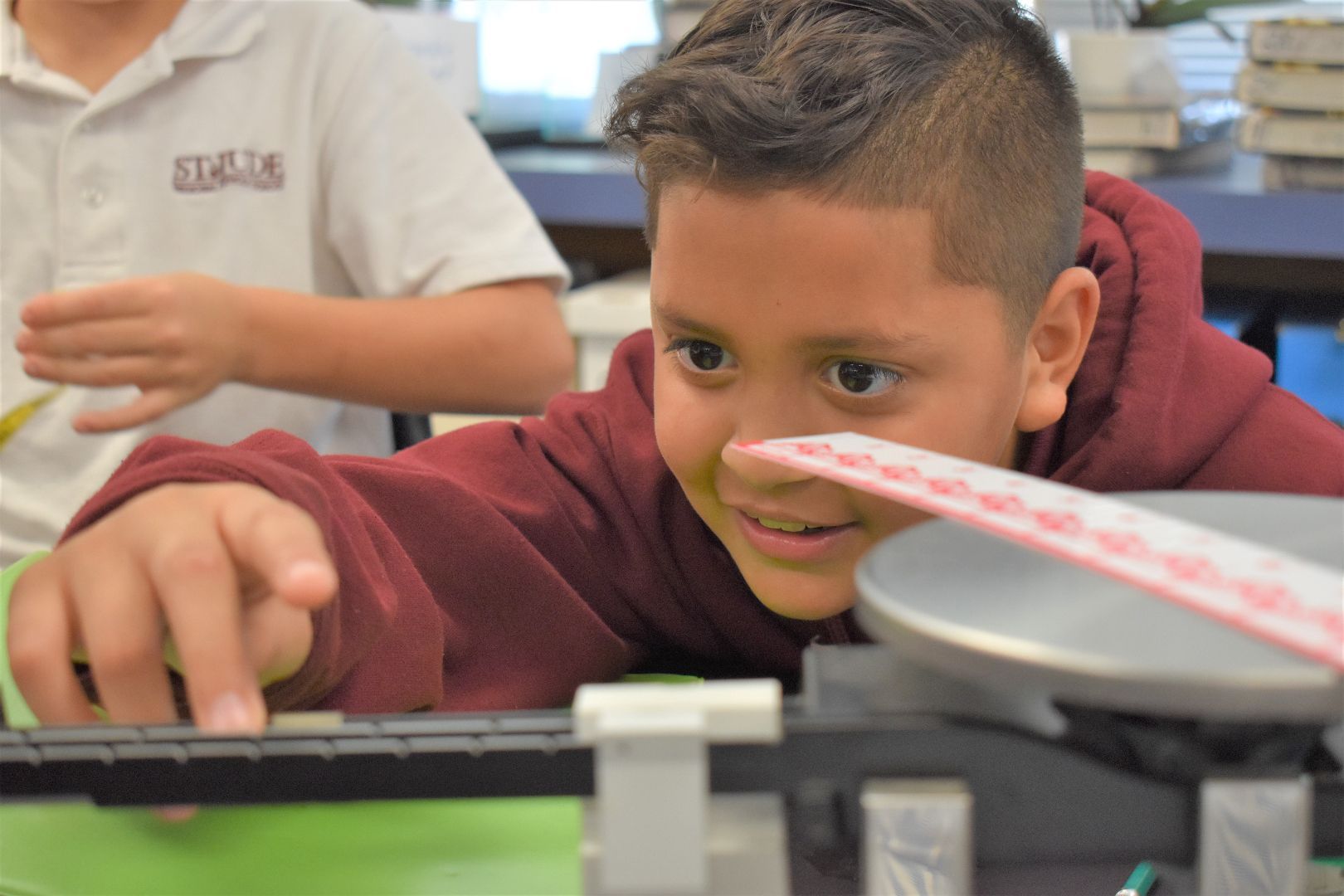 Child reaching toward a model train on a table in a classroom, focused and smiling