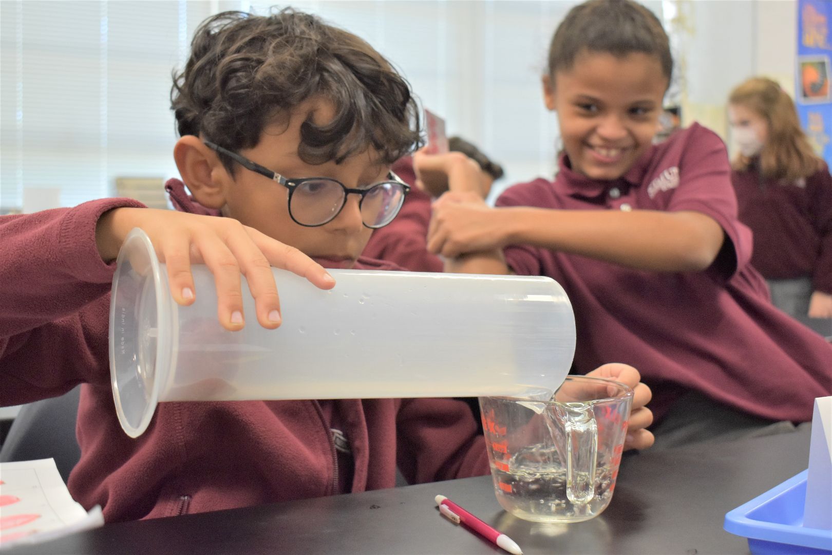 Student pours water from a measuring cup into a glass in a science classroom activity