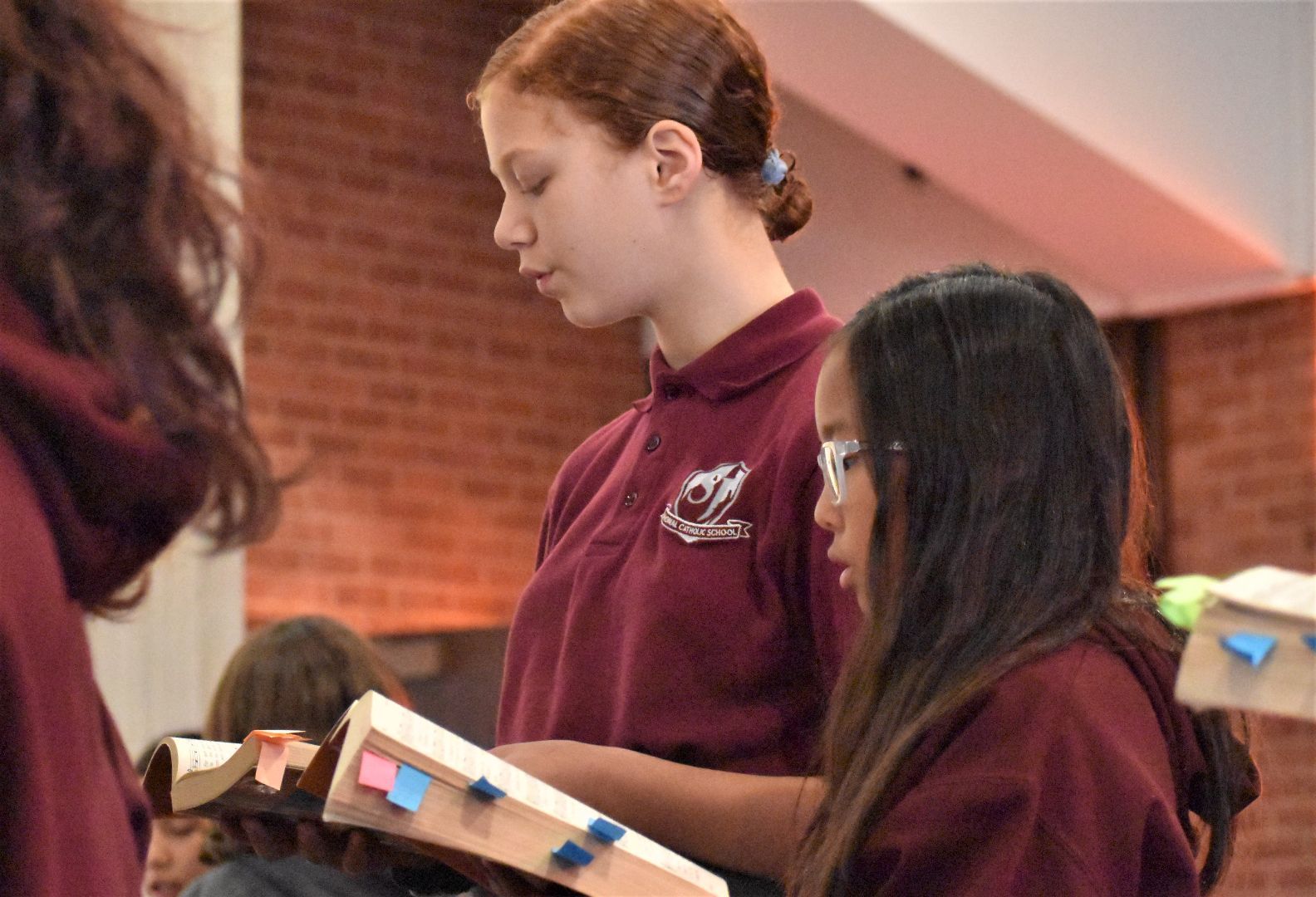 Students in maroon uniforms reading books in a classroom with brick walls