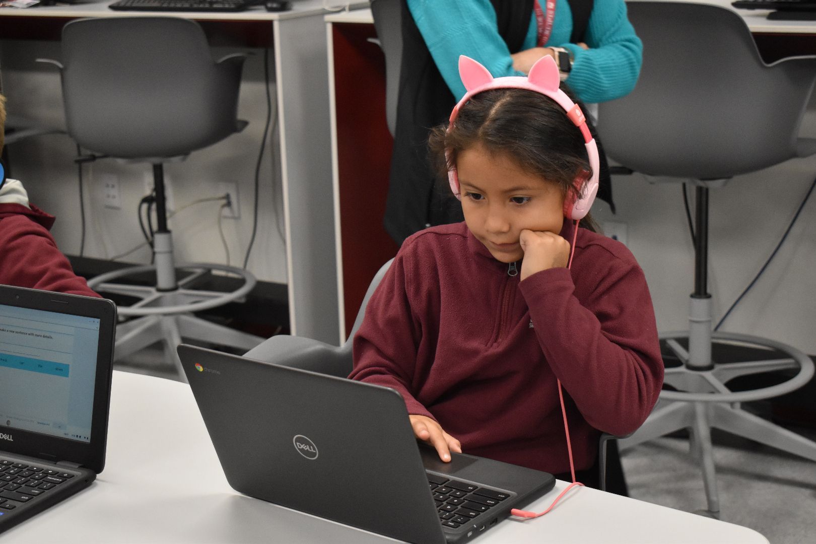 Student wearing headphones studies on a laptop in a classroom.