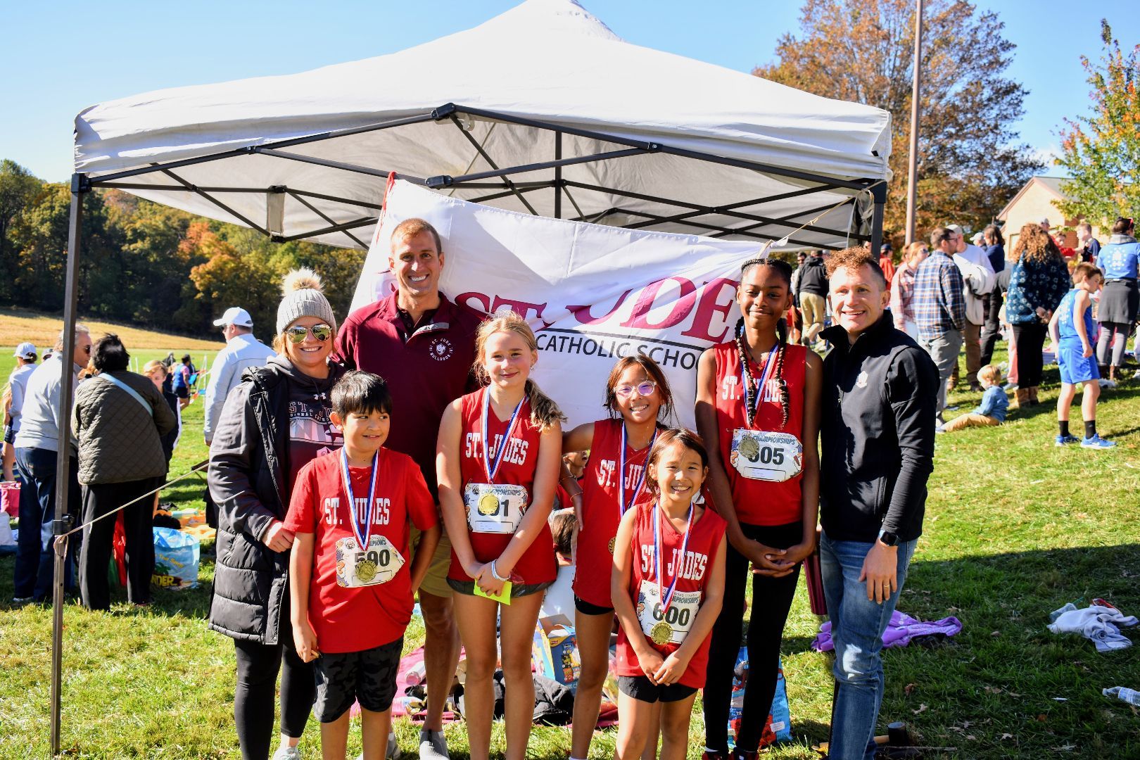 Children and adults posing in red shirts under a tent at an outdoor race event