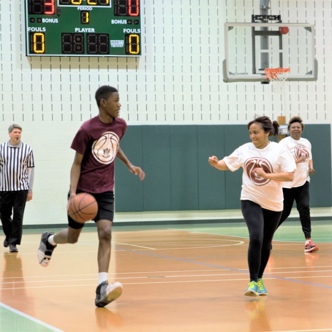 Basketball player dribbling in an indoor gym as a defender guards him near the hoop.