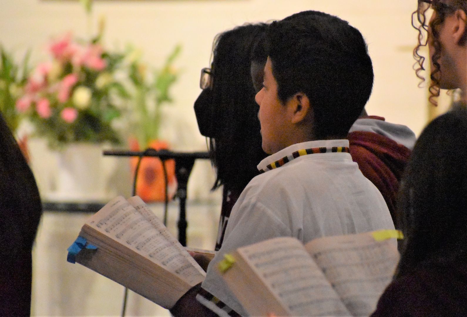 People seated in a church or choir setting, holding open music books during a service or rehearsal.