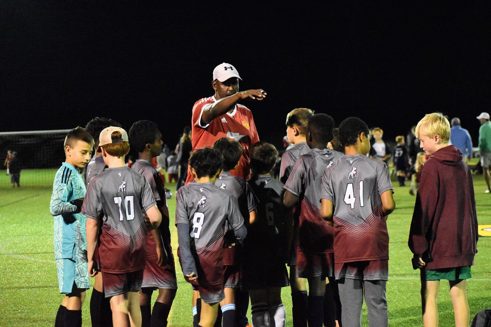 Soccer coach addressing a huddle of youth players on a field at night