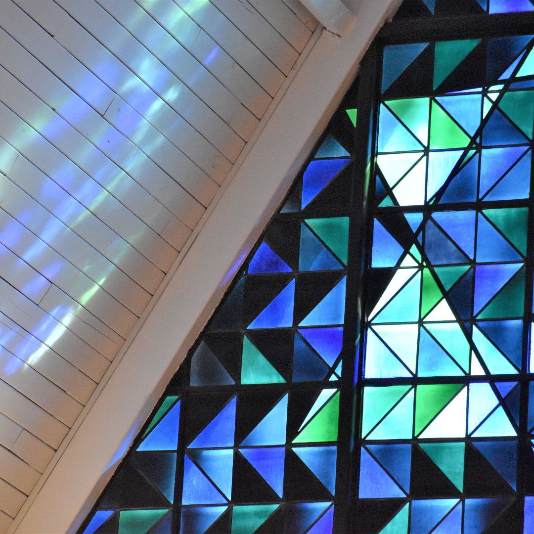 Abstract blue and green geometric stained glass beside a white paneled ceiling