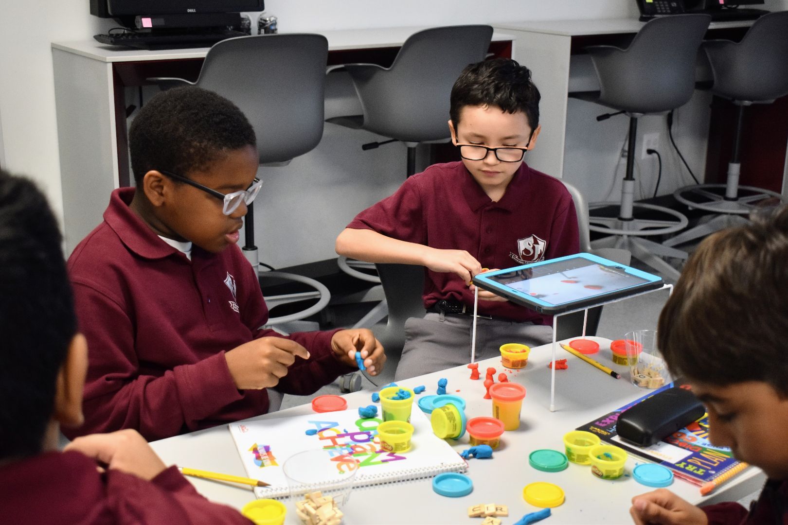 Children playing a colorful tabletop board game in a classroom, focused on the game pieces.