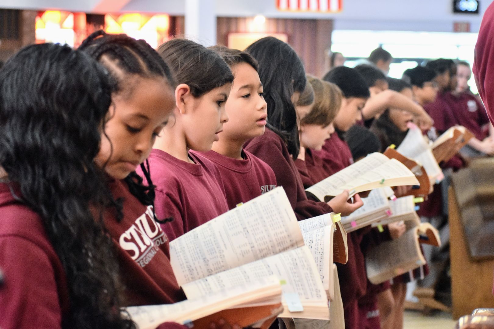 People standing in a line reading booklets at an indoor event