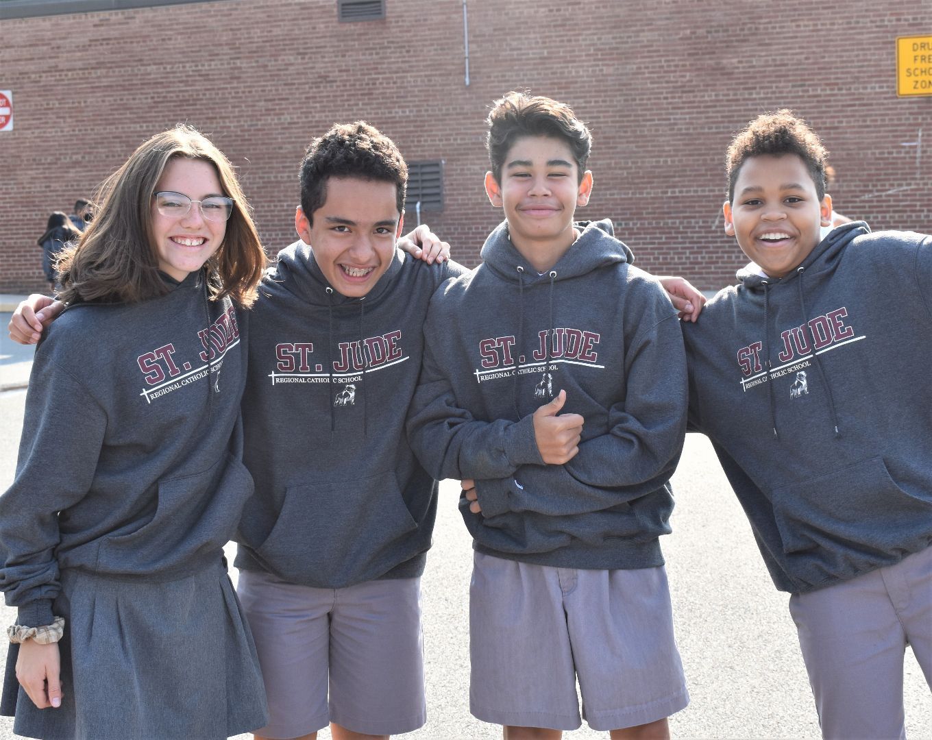 Four friends in matching hoodies smiling outdoors in front of a brick building